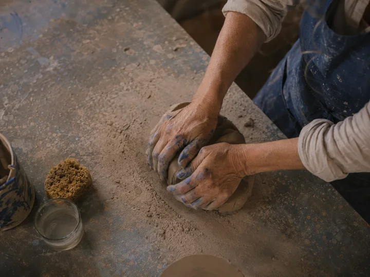Top-down view of Maria's hands wedging stoneware clay on the workbench.