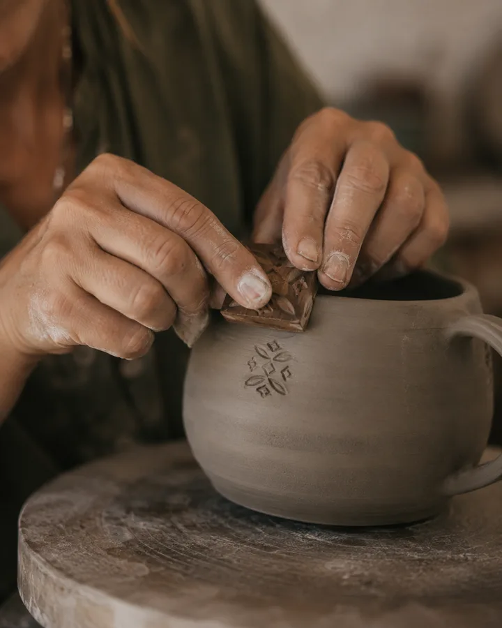 Zoé's hands pressing a wooden stamp into the side of a stoneware mug.