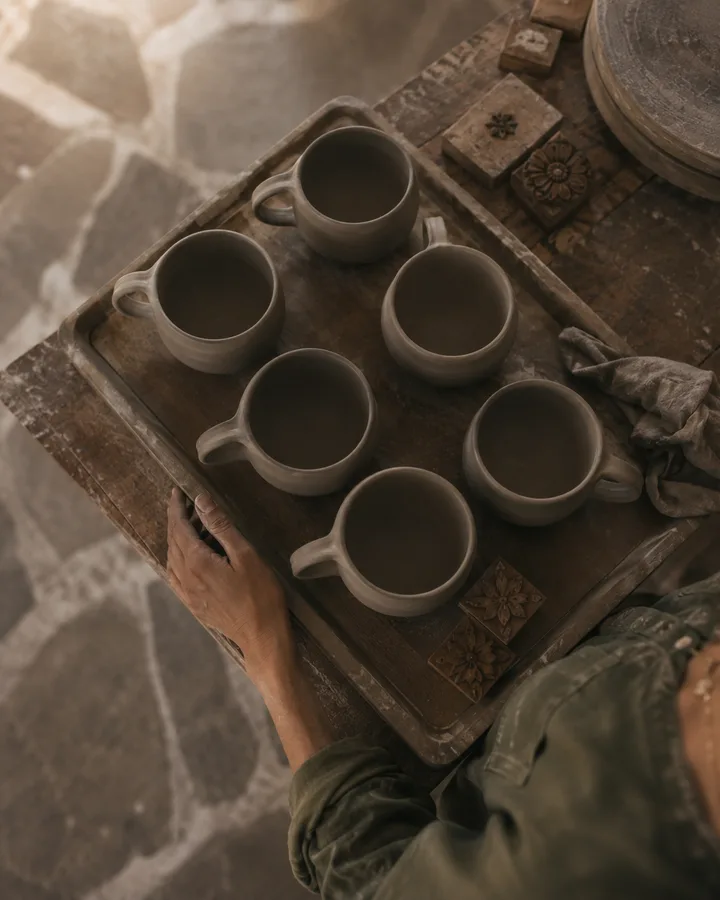 Tray of leather-hard mugs and carved wooden stamps on Zoé's workbench.